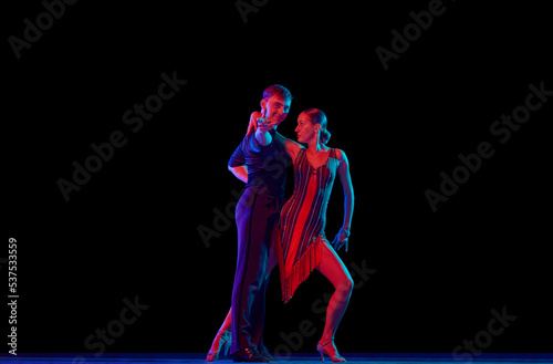 Two dancing people, ballroom dancers in elegance outfits in motion, action over dark background in neon light. Concept of art, music, dance, emotions.