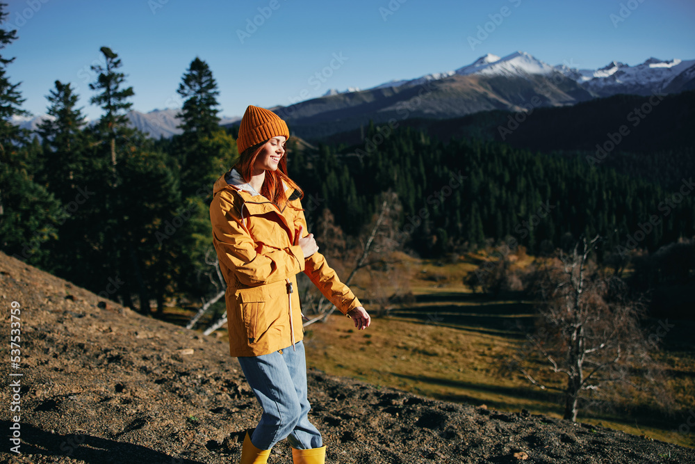 Woman full-length hiker smiling with teeth standing frozen on the mountain looking at nature happiness mountains and trees in yellow raincoat travel and hiking in the mountains at sunset freedom
