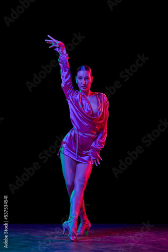 Fototapeta Naklejka Na Ścianę i Meble -  Queen. Portrait of young graceful flexible woman dancing ballroom dance without partner isolated on dark background in neon light.