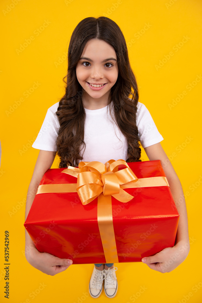 Happy teenager, positive and smiling emotions of teen girl. Teenager child in t shirt holding gift box on yellow isolated background. Gift for kids birthday. Summer holiday. Happy teenager, positive and smiling emotions of teen girl. Teenager child in t shirt holding gift box on yellow isolated background. Gift for kids birthday. Summer holiday.