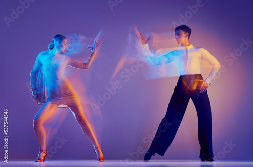 Art in motion. Flexible adorable ballroom dancers in stage attires dancing isolated on purple background in neon mixed light. Music, dance, emotions © master1305