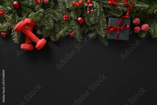 Fototapeta Naklejka Na Ścianę i Meble -  Christmas sport composition with gift and two red sports dumbbells on black background. Top view with copy space. Fitness, sport and healthy concept. Christmas greeting card. Winter sale.