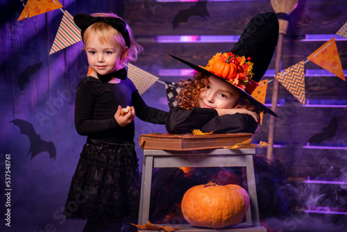 Happy Halloween. Two cute cheerful little witches with a magic wand and a book of spells conjure.