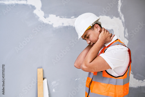 A young Asian construction worker holds his neck in pain from workplace injury