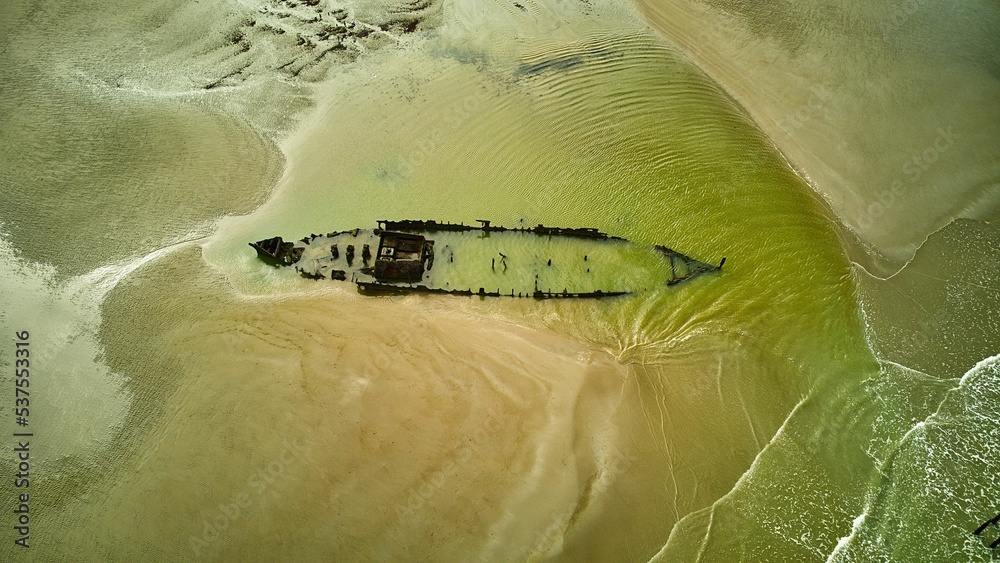 Naklejka premium Aerial view of shipwreck in the shallow green sea water by the sandy beach