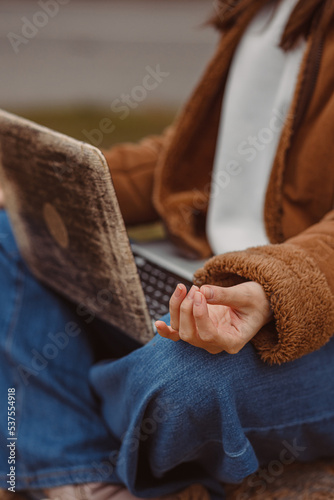 Crop female freelancer with yoga mudra sitting with laptop and meditating during break in work in nature 