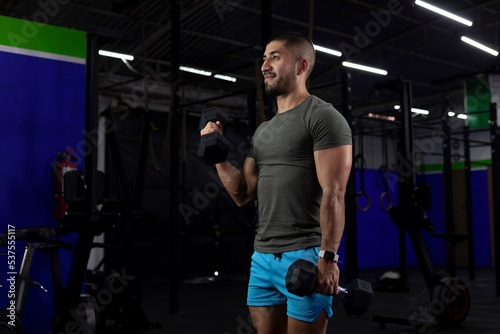 vertical image of a latin athlete, doing bicep exercises with two dumbbells in a gym