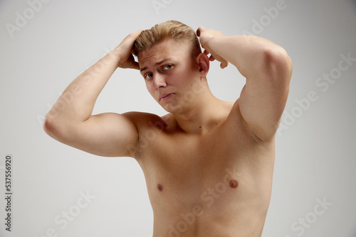 Portrait of young man posing shirtless isolated over grey studio background. Doing hairstyle with wax styler