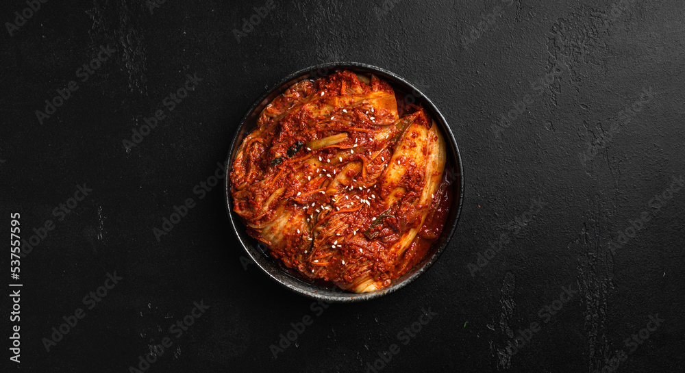 Kimchi in a black bowl on a black background, traditional Korean food, top view, copy space  - obrazy, fototapety, plakaty 