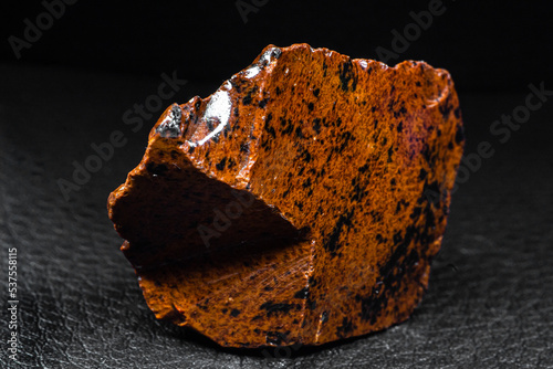 Real shiny specimen of orange Mahogany Obsidian volcanic stone macro isolated on black leather background photo