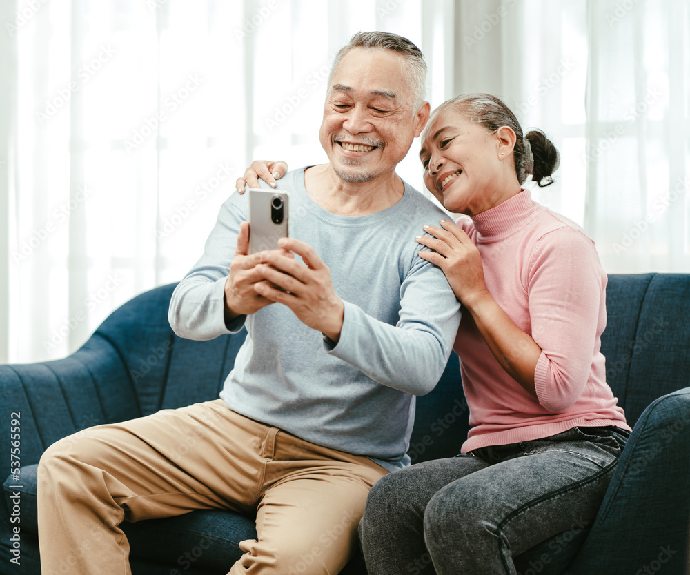 Happy Asian senior couple doing family online call via internet connection using mobilephone smiling. Elderly husband and wife talking on video call. Pensioner and modern communication technology. Happy Asian senior couple doing family online call via internet connection using mobilephone smiling. Elderly husband and wife talking on video call. Pensioner and modern communication technology.