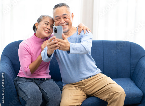 Happy Asian senior couple doing family online call via internet connection using mobilephone smiling. Elderly husband and wife talking on video call. Pensioner and modern communication technology.