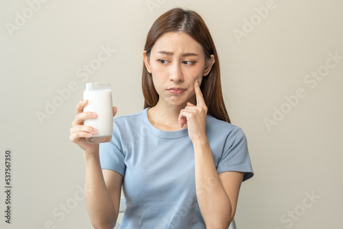 Foto Allergy asian young woman, girl looking, holding glass of milk, face in thinking before drink milk as it may upset her stomach ache, pain