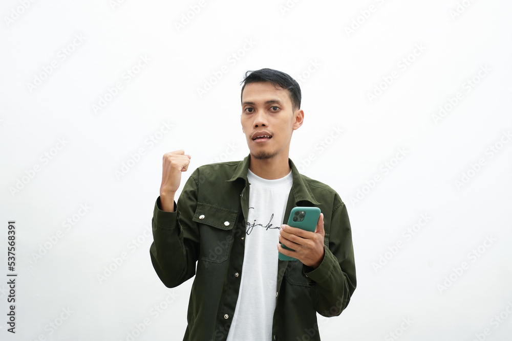 Asian man wearing casual green shirt looking at smartphone screen with shocked, surprised, dumbfounded expression. isolated white background Asian man wearing casual green shirt looking at smartphone screen with shocked, surprised, dumbfounded expression. isolated white background