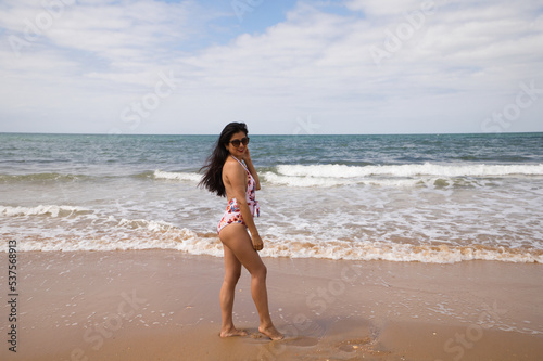 Beautiful and young latin woman is walking along the shore of the beach and posing for photos. Beautiful woman is on holiday on a paradise beach. Holiday and travel concept.