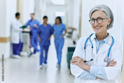 Mature female general practitioner with stethoscope standing in medical clinic or hospital, portrait. Health professional while working day