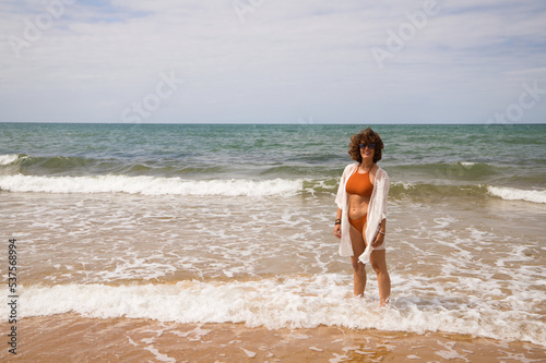 Young beautiful woman in bikini walking along the beach shore. The woman is enjoying her trip to a paradise beach while making different gestures and expressions. Holidays and travels.