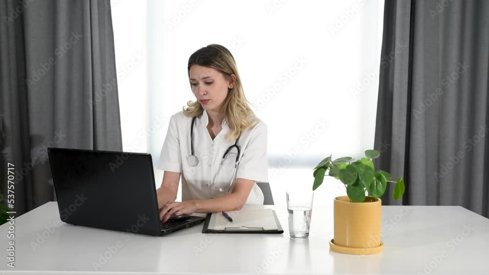 Serious young woman doctor physician wearing white coat using laptop computer writing notes at workplace. Female professional medic consulting patient distantly in online chat sit at desk in hospital. Serious young woman doctor physician wearing white coat using laptop computer writing notes at workplace. Female professional medic consulting patient distantly in online chat sit at desk in hospital.