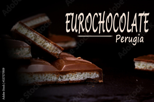 Pieces of milk aerated chocolate close-up on a dark background with an inscription. The concept of the Perugia Chocolate Festival