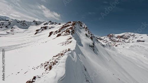 Aerial view flight climbing mountain summit cliff texture snow reversal dive from top ridge alpine sunny landscape. FPV sports drone epic rock scenery skyline panorama wild hilly valley freeze glacier