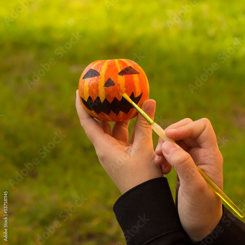 Preparation for Halloween girl hands paint orange pumpkin with black paint. Holiday decoration concept