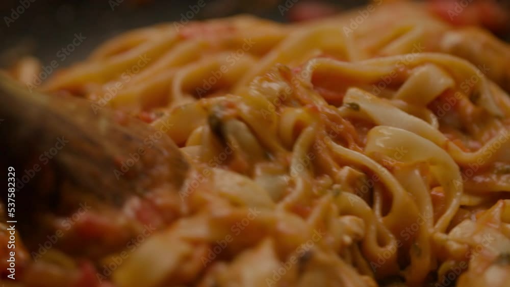 Fettuccine pasta mixing with tomato sauce on frying pan in slow motion, close up. Fettuccine pasta mixing with tomato sauce on frying pan in slow motion, close up.
