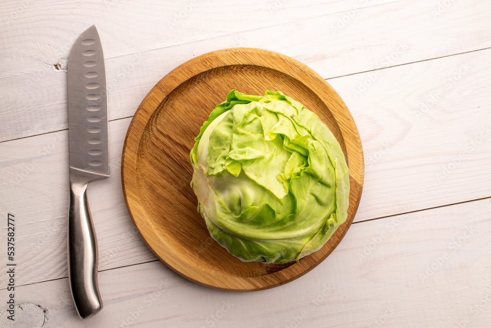 One fresh juicy organic cabbage on a round wooden tray with a metal knife, close-up, on a wooden table, top view. One fresh juicy organic cabbage on a round wooden tray with a metal knife, close-up, on a wooden table, top view.