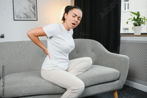 Sad young woman touching back feeling backache morning discomfort low lumbar muscular kidney pain sit on bed after waking up Concept of woman stretching suffering from sudden back pain