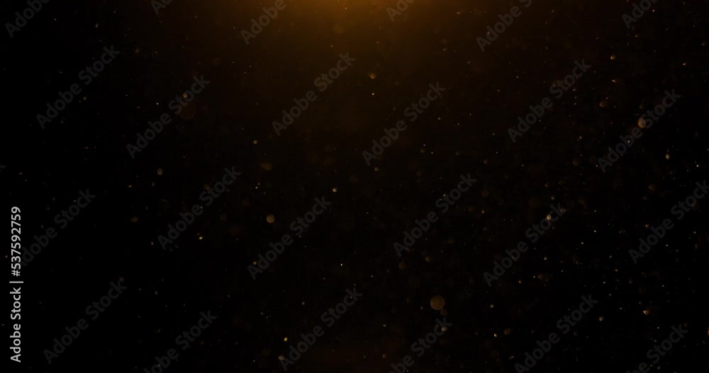 Gold particles flying in wind on black background, depth of field. Golden glitter slow motion in spot light. Dust particles 4k overlay video. Beautiful bokeh abstract background. 