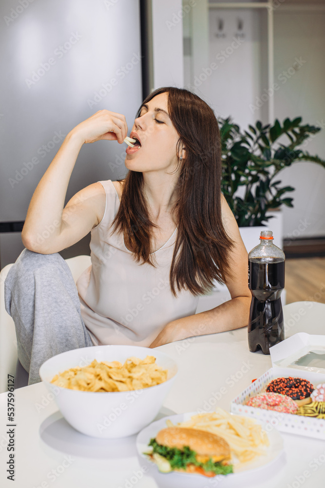 A woman eats junk food at home in the kitchen.