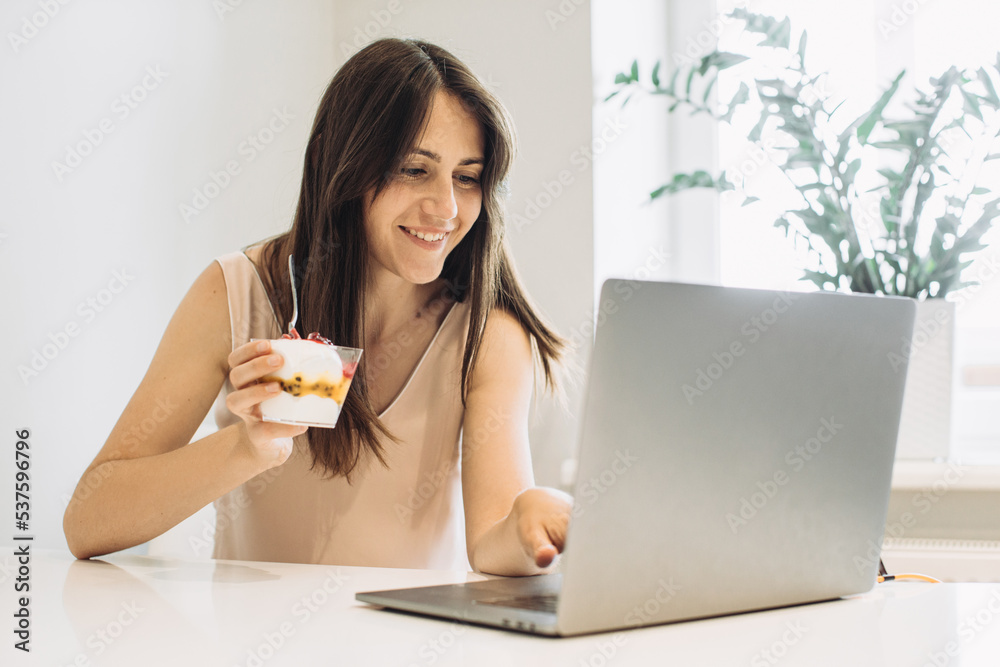 The concept of working at home. Young woman with a laptop in the kitchen, working with pleasure and eating delicious ice cream. The concept of working at home. Young woman with a laptop in the kitchen, working with pleasure and eating delicious ice cream.