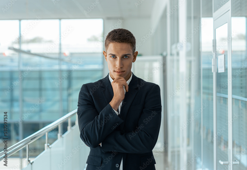Young male consultant standing in auto show office and looking at camera Young male consultant standing in auto show office and looking at camera