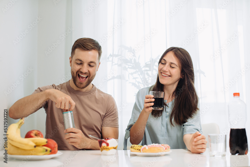 Breakfast in the kitchen. A couple eats donuts and sweets, junk food concept. Breakfast in the kitchen. A couple eats donuts and sweets, junk food concept.