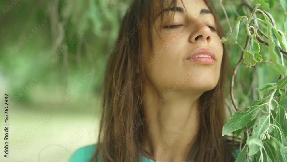 Candid portrait of attractive brunette woman smiling to camera and looking happy, standing at green olive tree. girl in turquoise sweatshot playing with leaves. natural look concept Candid portrait of attractive brunette woman smiling to camera and looking happy, standing at green olive tree. girl in turquoise sweatshot playing with leaves. natural look concept