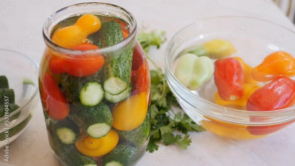 A glass jar filled with cucumbers and bright yellow and red organic tomatoes filled with marinade for canning. Bowls on the table with tomatoes and cucumbers, dolly shot. Canned vegetables A glass jar filled with cucumbers and bright yellow and red organic tomatoes filled with marinade for canning. Bowls on the table with tomatoes and cucumbers, dolly shot. Canned vegetables