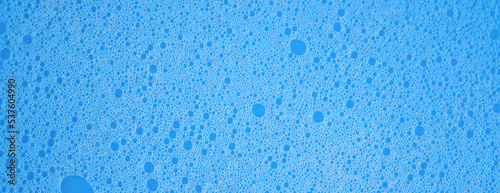 Macro photo of white shampoo or detergent foam on blue background, banner