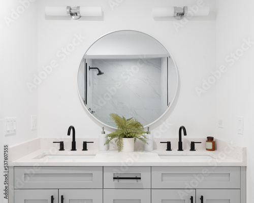 Fotobehang A renovated bathroom with a grey vanity cabinet, circular mirror with a view to a shower, and back faucets