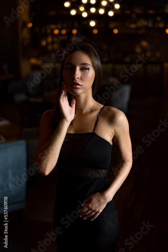 A young attractive woman in a black dress holds her hands near her face. Mysterious woman in thought.