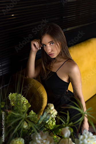 portrait of a young attractive woman in a black dress sitting on a sofa looking at the camera.
