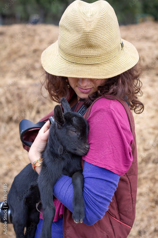 Female with hat on hugging a very young goat in her arms. Female with hat on hugging a very young goat in her arms.