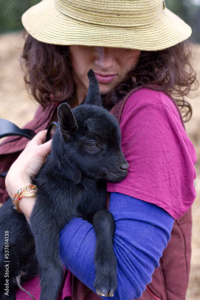 Close up of female with hat on hugging a very young goat in her arms. Close up of female with hat on hugging a very young goat in her arms.