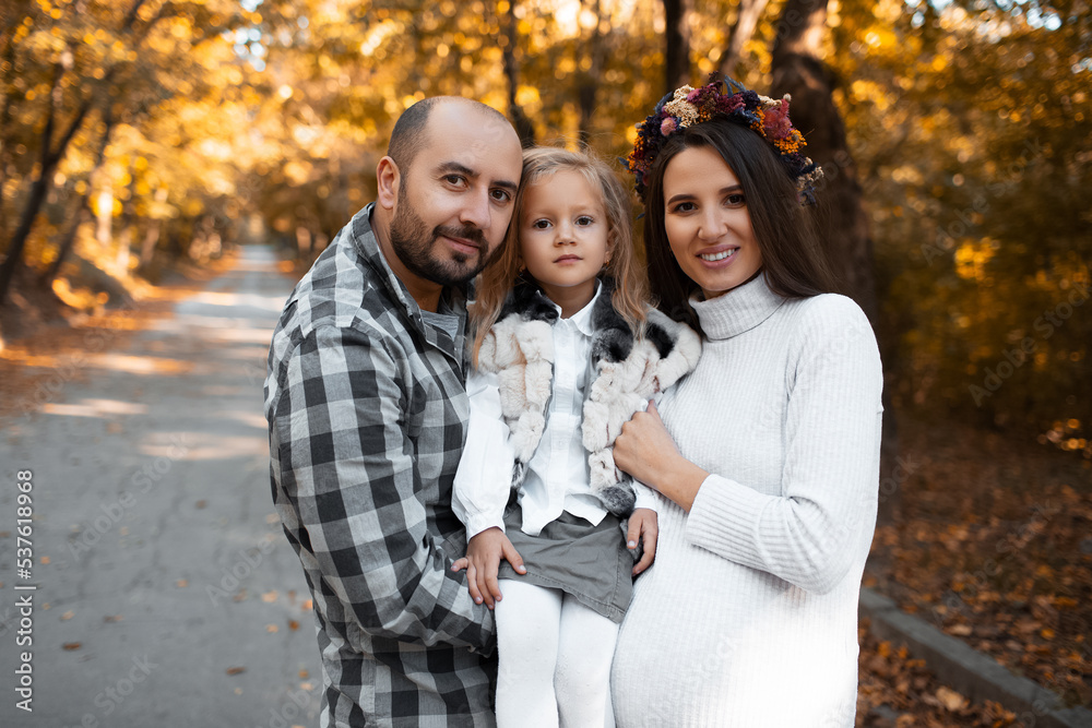 Portrait of happy family on background of golden park in autumn day. Father, daughter and pregnant mother. Portrait of happy family on background of golden park in autumn day. Father, daughter and pregnant mother.