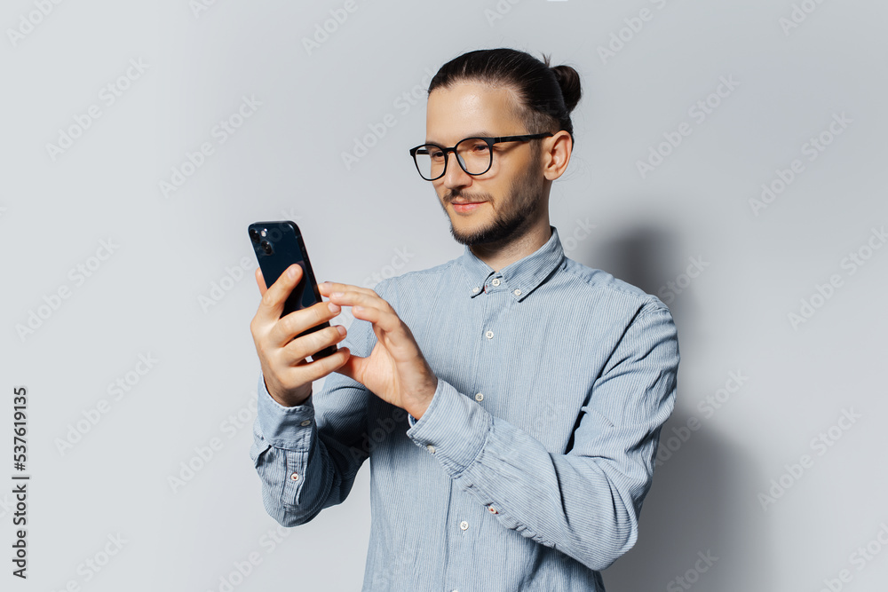 Studio portrait of young man using smartphone on white background, wearing blue shirt and eyeglasses. Studio portrait of young man using smartphone on white background, wearing blue shirt and eyeglasses.