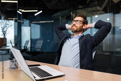 Photography Completion work important project, mature man working inside modern office building using laptop, senior boss with beard and glasses putting hands behind head dreaming and visualizing future plans