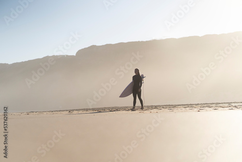 Surfer girl at the beach with her surfboard at sunset time. Female surfer