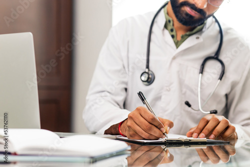 indian doctor wearing uniform taking notes in medical documents photo