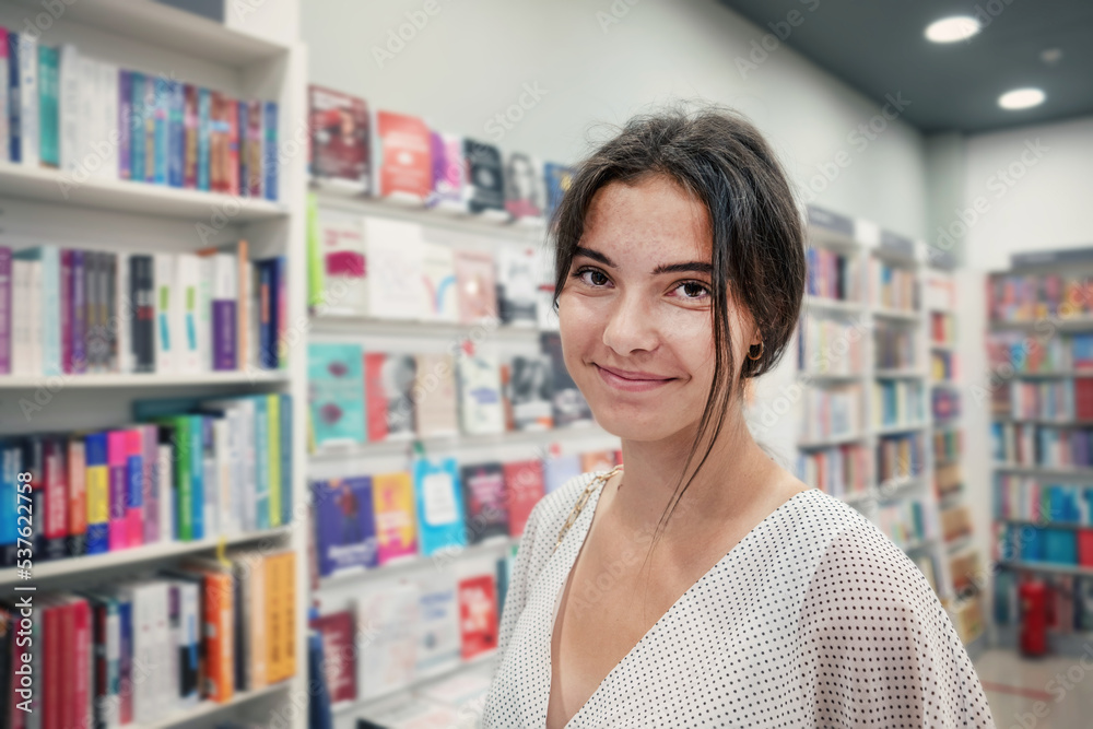 Authentic portrait of smiling teenage female student standing in library of university inside Authentic portrait of smiling teenage female student standing in library of university inside
