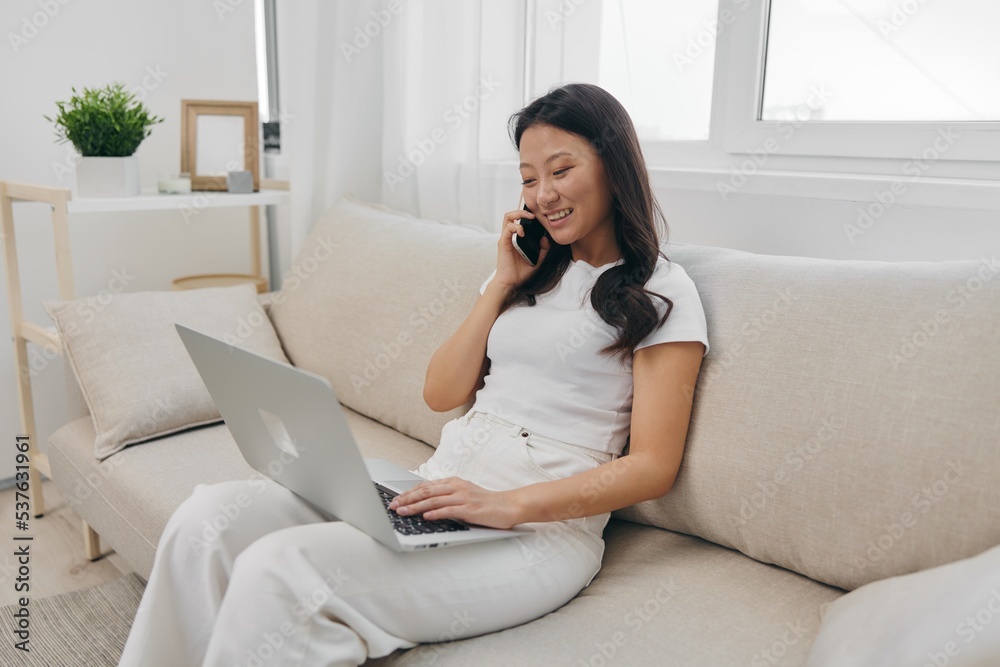 Asian woman sitting with laptop and phone in freelancer's home office looking at laptop screen with headphones working, lifestyle work and home Asian woman sitting with laptop and phone in freelancer's home office looking at laptop screen with headphones working, lifestyle work and home