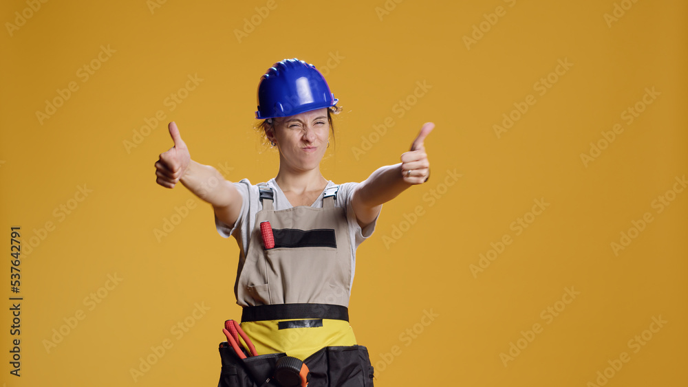 Portrait of female construction worker giving thumbs up in studio, showing approval and agreement on camera. Woman builder doing like and satisfaction gesture, good renovation work. Portrait of female construction worker giving thumbs up in studio, showing approval and agreement on camera. Woman builder doing like and satisfaction gesture, good renovation work.