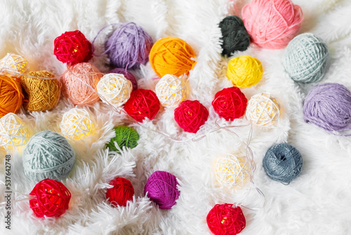 Bright multicolored knitting yarn and a luminous garland in the form of balls lie on fluffy blanket.